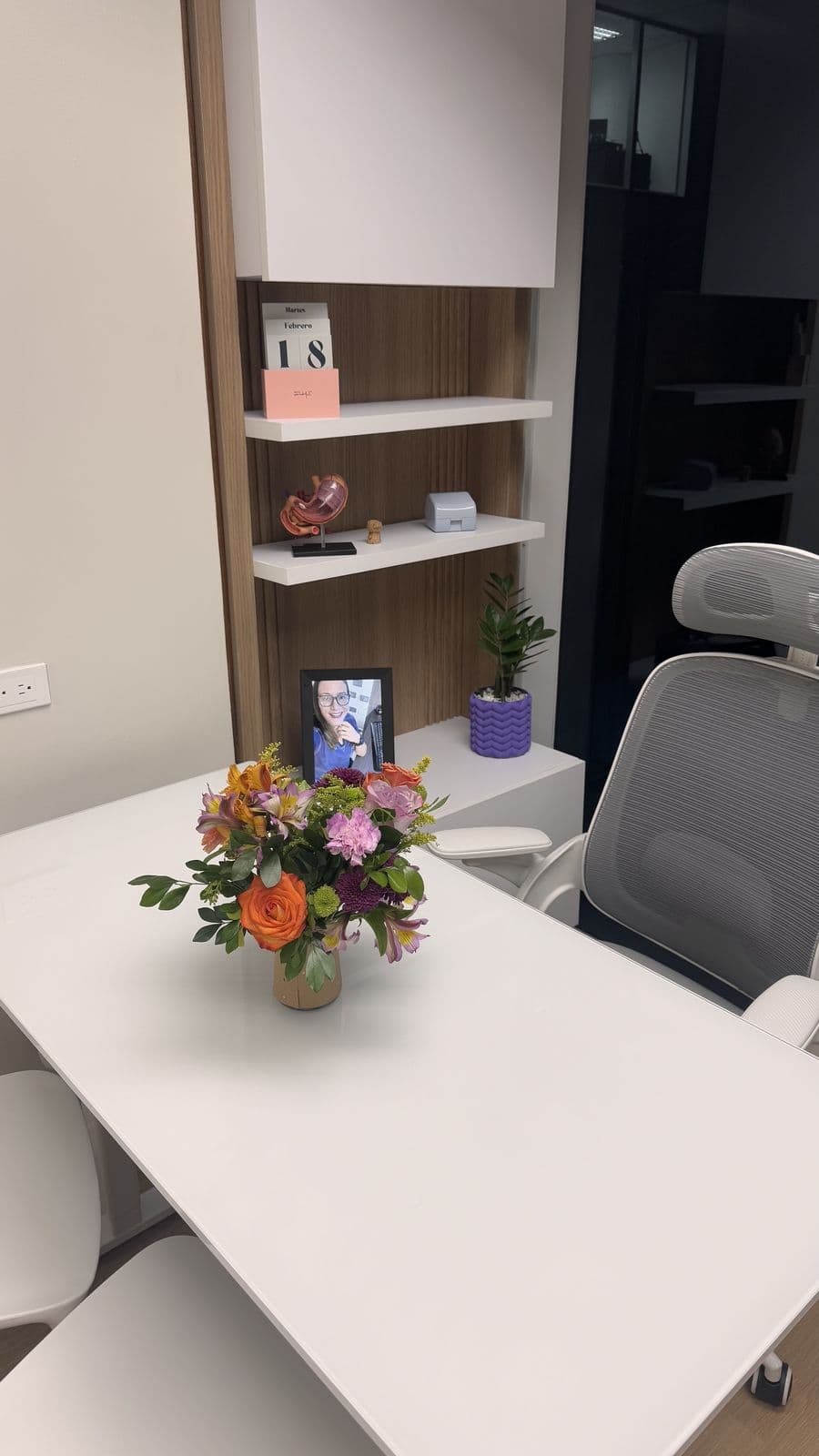 Consultorio de Gastrolozada: escritorio blanco con flores, sillas y repisas decoradas