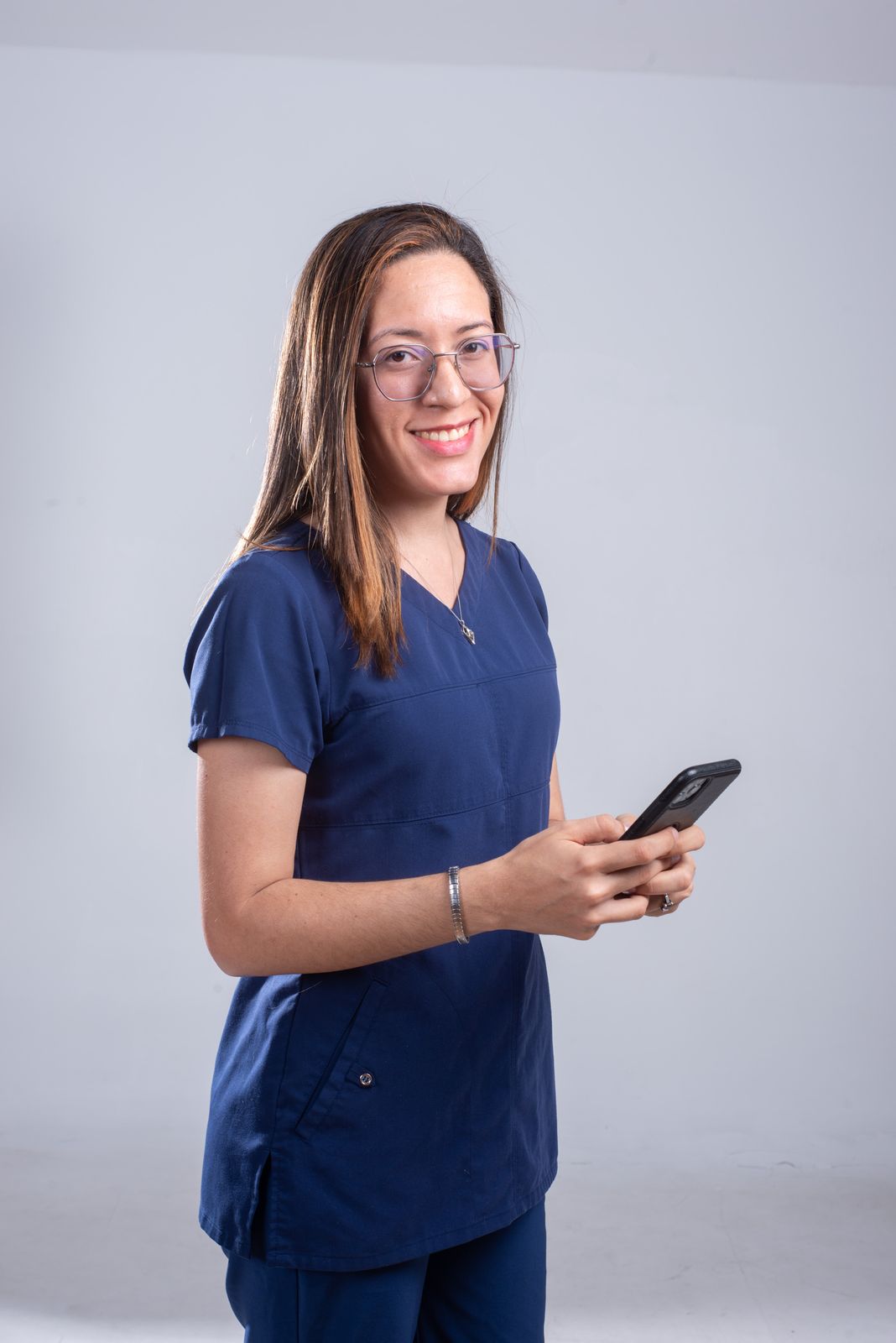 La Dra. Yraili Lozada con uniforme quirúrgico azul, sonriendo con el teléfono en la mano